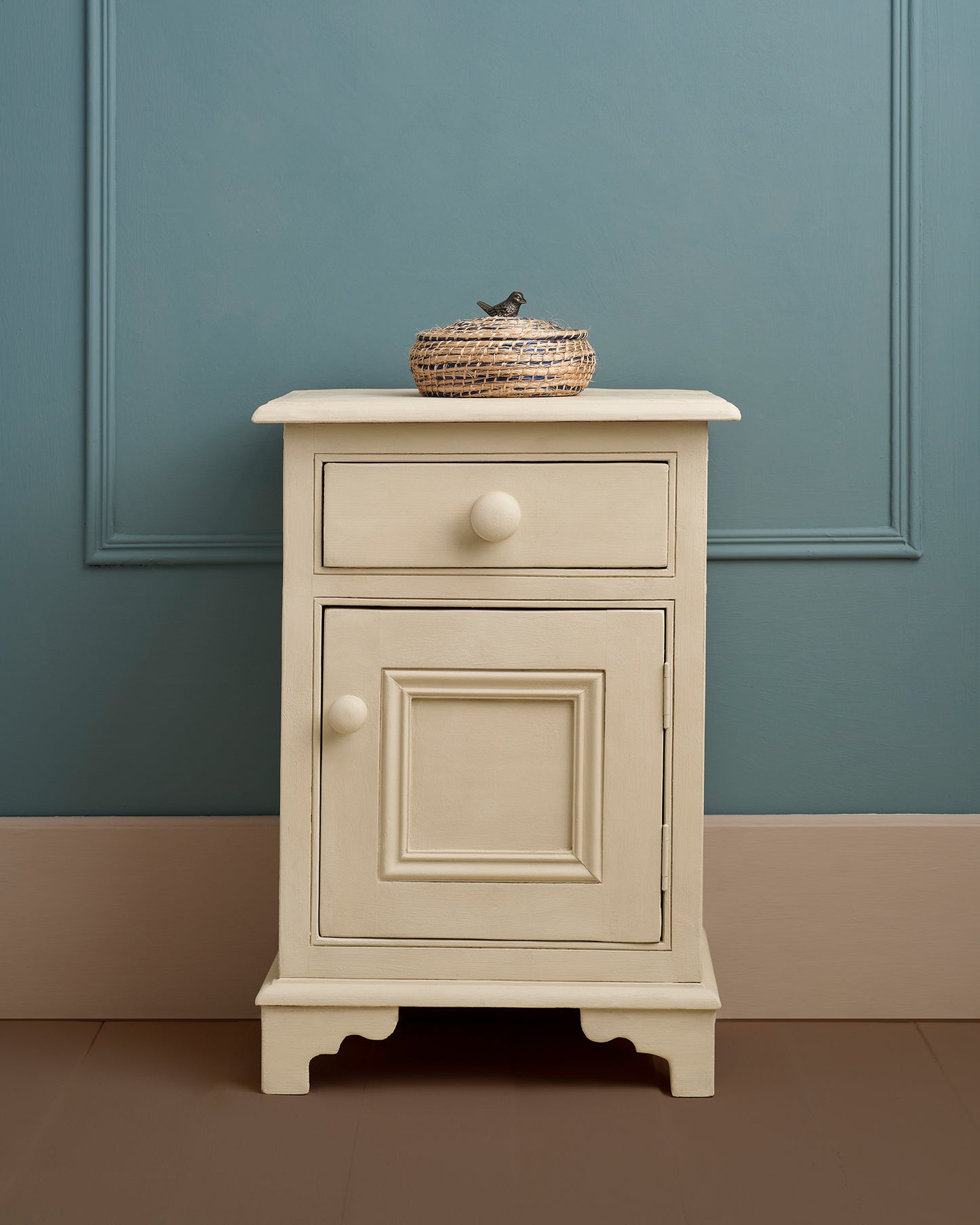 Beige nightstand with a single drawer and cabinet against a teal wall.