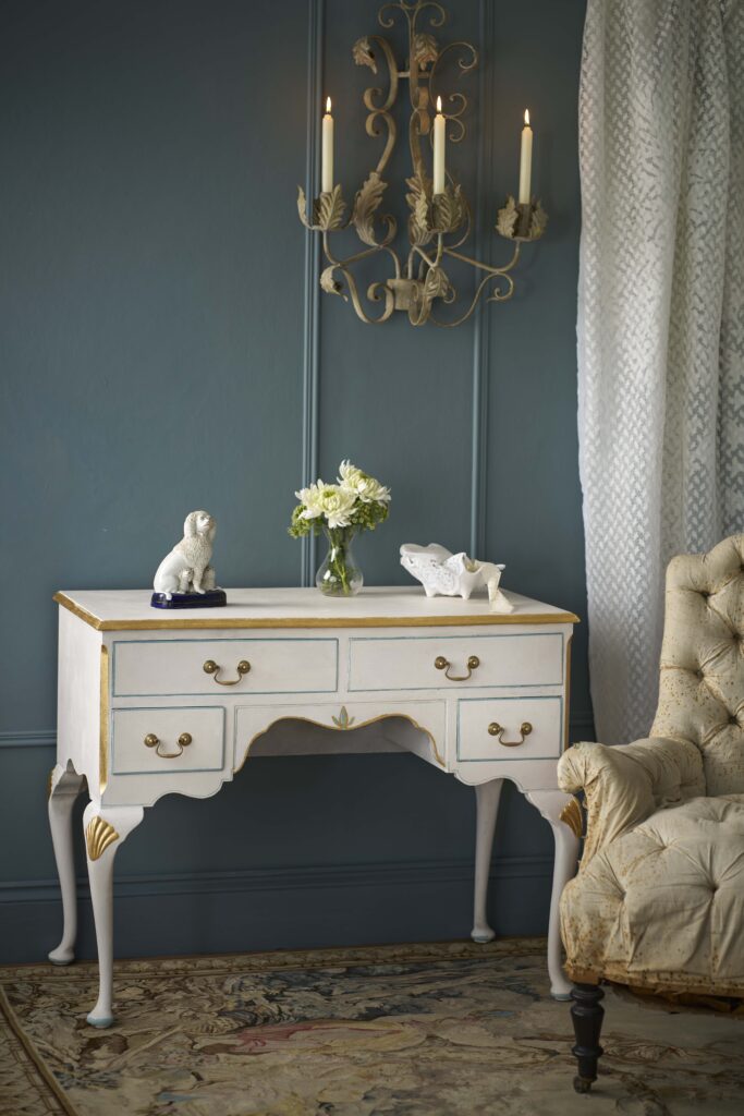 White dresser painted with Annie Sloan Chalk Paint in colour Rococo White with gold accents in a room with a chandelier and decorative items.