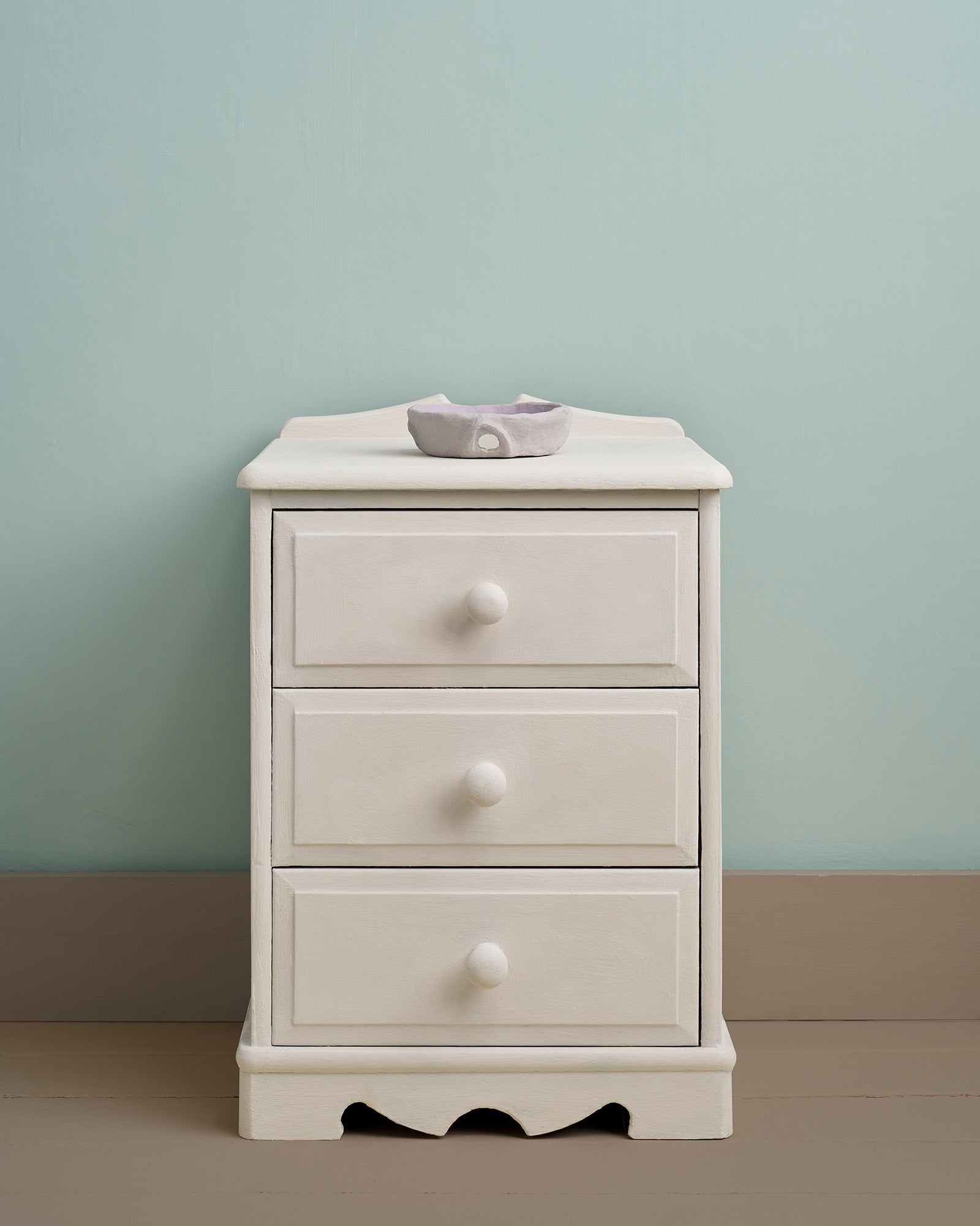 White three-drawer nightstand against a light green wall